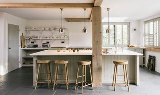 White kitchen with timber beams, open shelving and wooden stools at an island painted with off white accents.