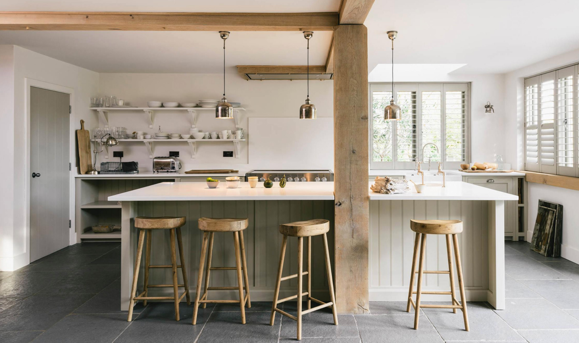 White kitchen with timber beams, open shelving and wooden stools at an island painted with off white accents.