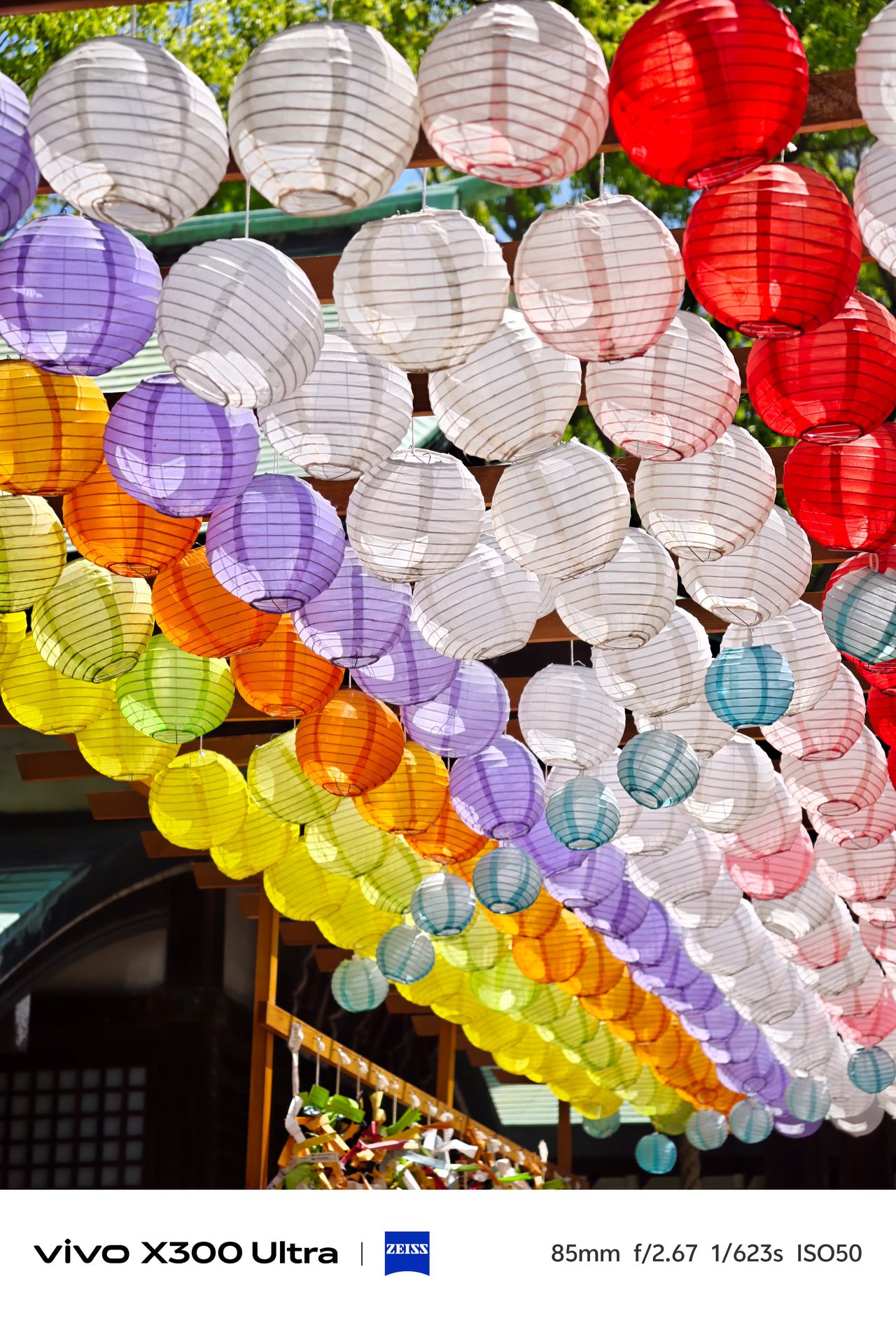 Hundreds of colorful paper lanterns in shades of white, red, purple, and yellow hanging overhead.