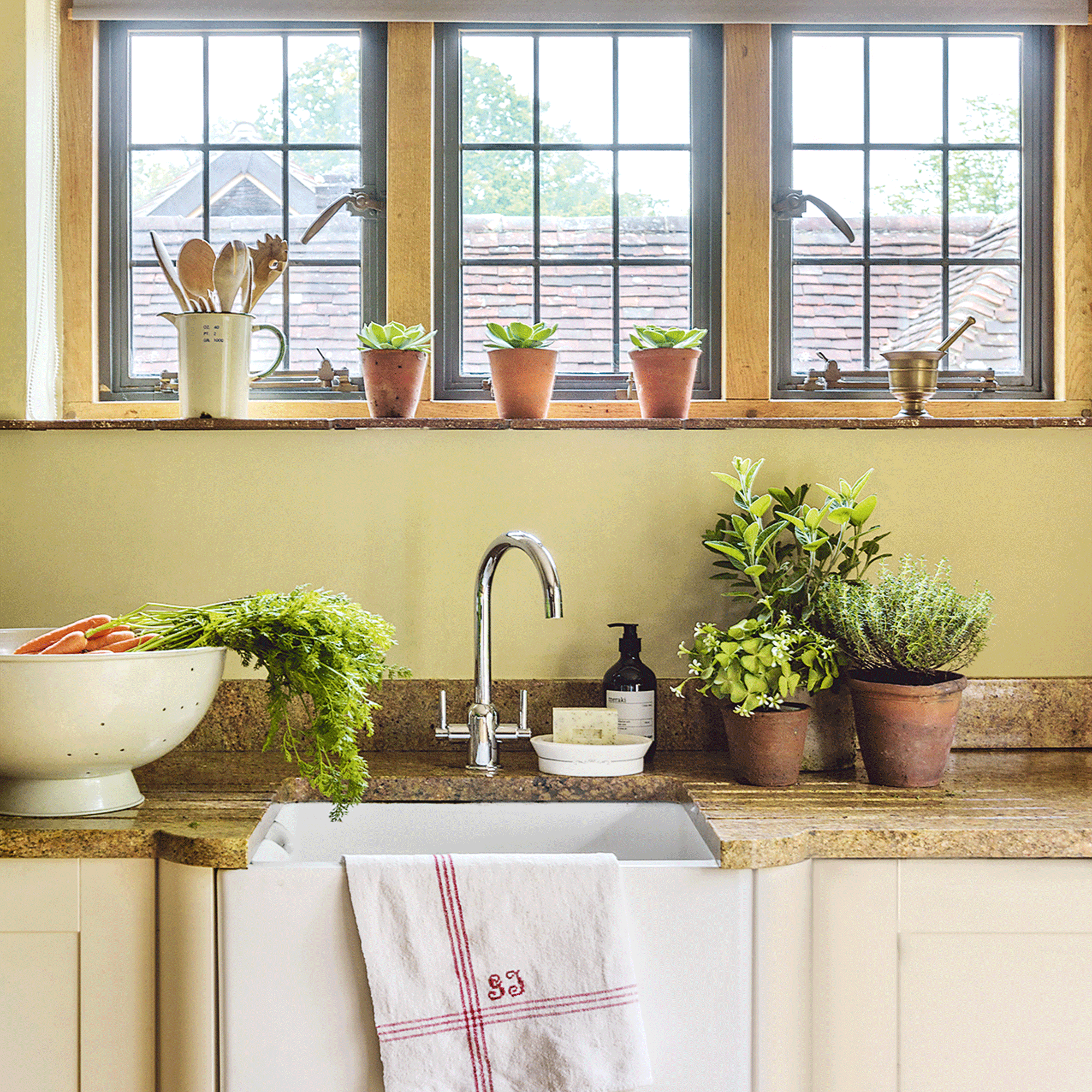 Sink in yellow kitchen with herbs in plant pots