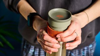 Twisting up the Wacaco Pipamoka portable coffee maker in front of a blue background.