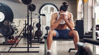 A man wiping sweat from his brow in the gym with his t-shirt