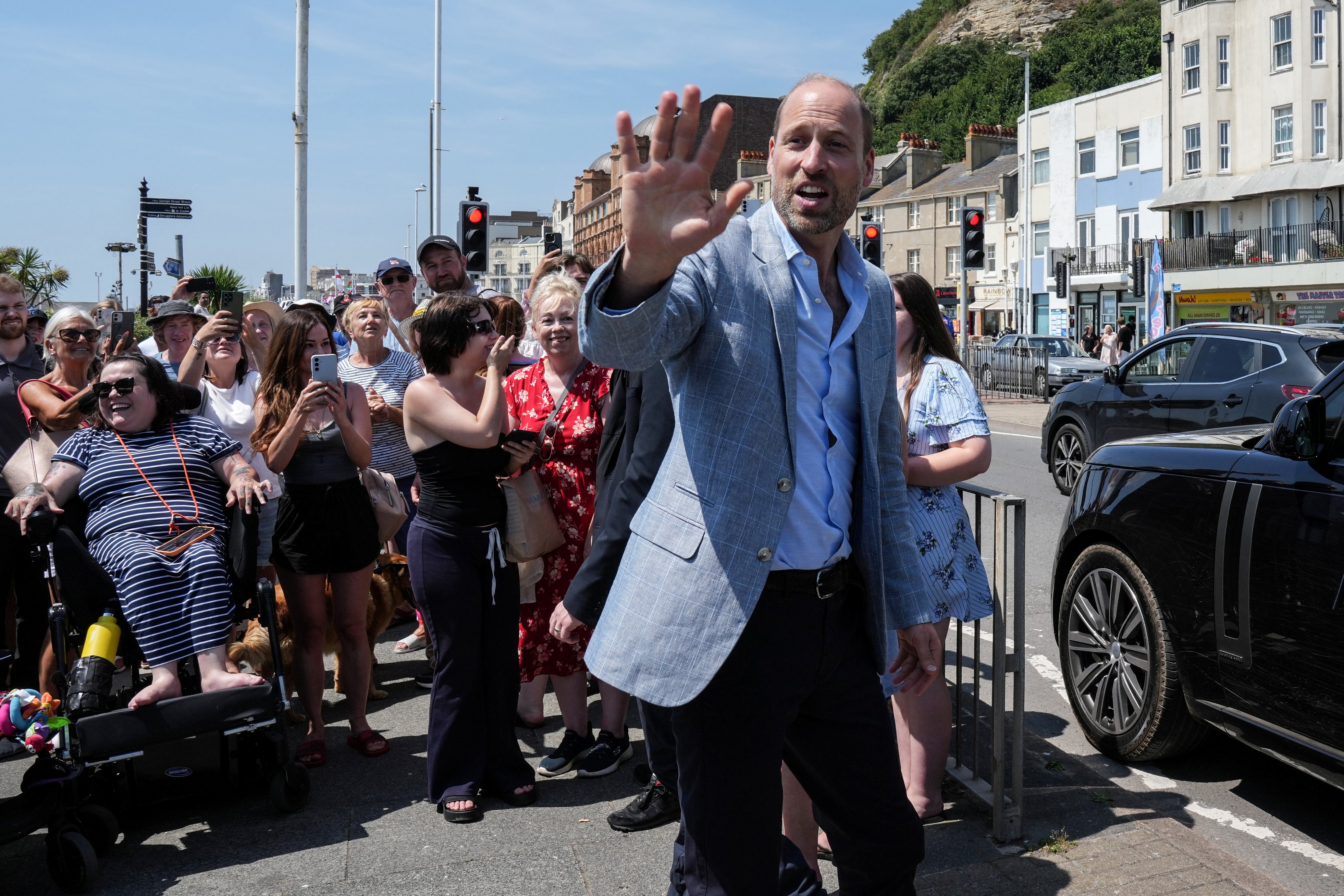 Prince William wears a gray suit jacket, a blue shirt and black slacks to visit Hastings, where he meets children and royal fans on the seafront