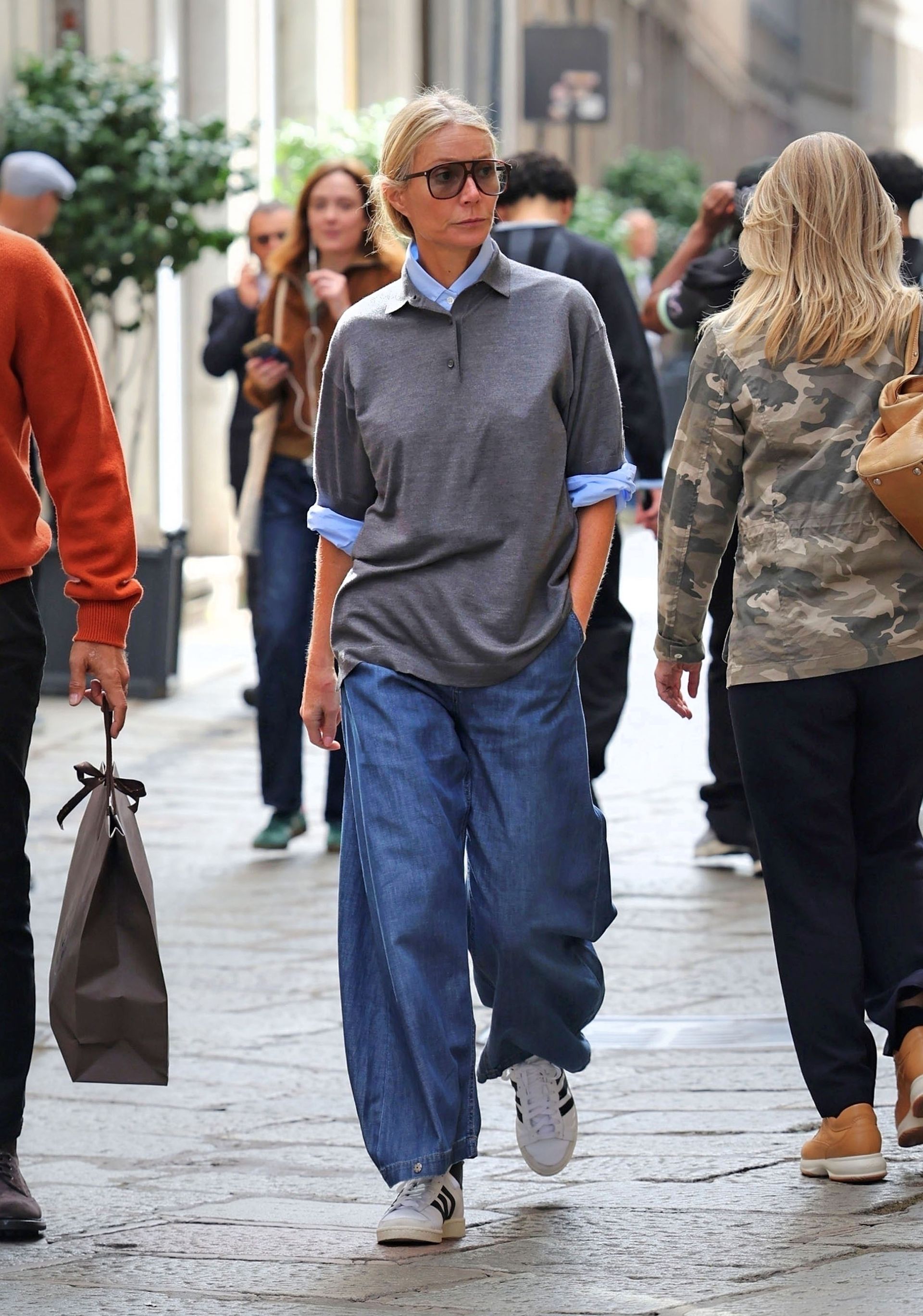 Gwyneth Paltrow wears a gray polo sweater over a blue button down with baggy blue jeans and Adidas high-top sneakers.