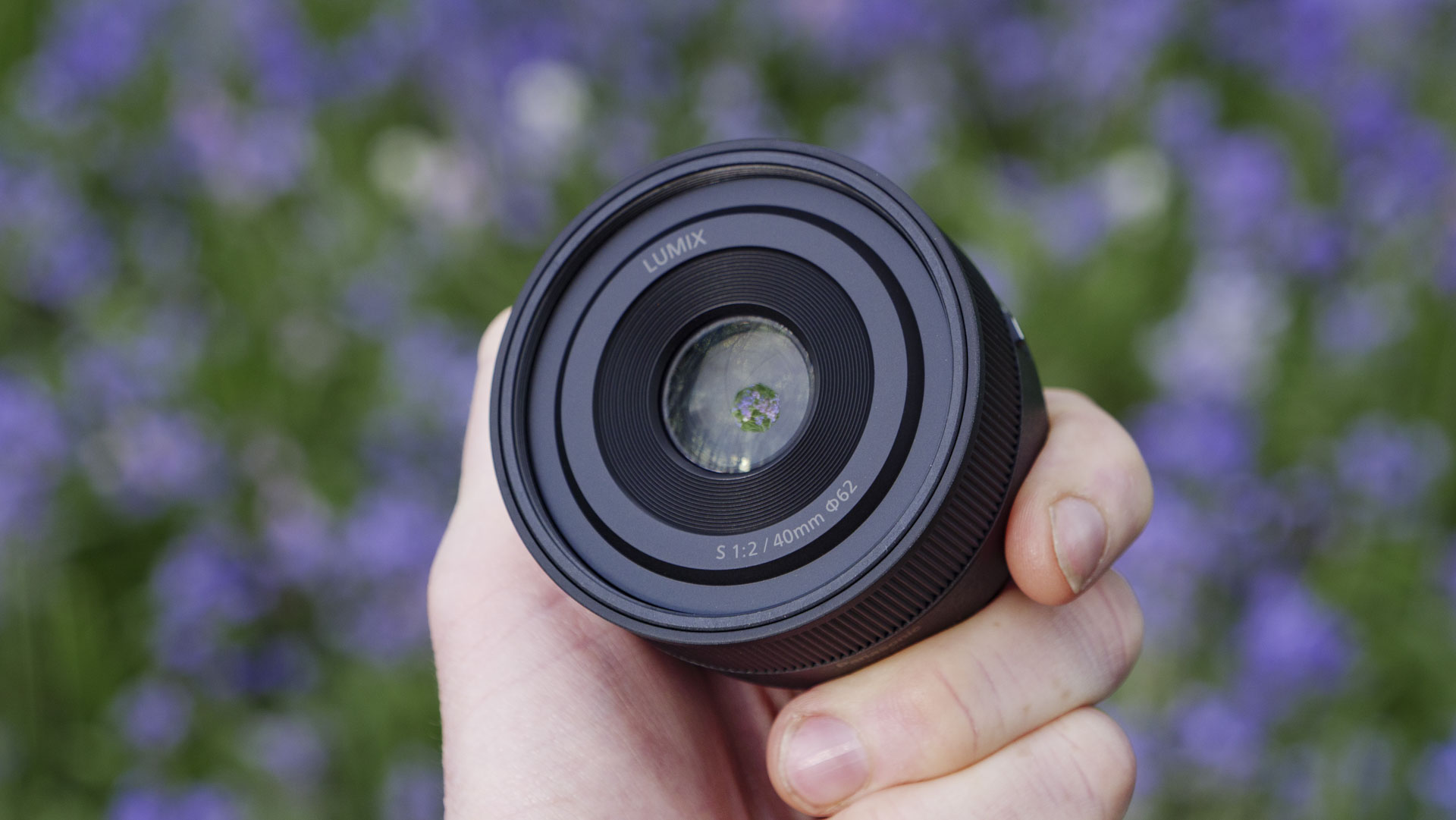 The Panasonic Lumix S 40mm F2 lens in the hand, with natural bluebell backdrop