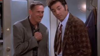 Mark Metcalf and Michael Richards talking to each other in a doorway on Seinfeld