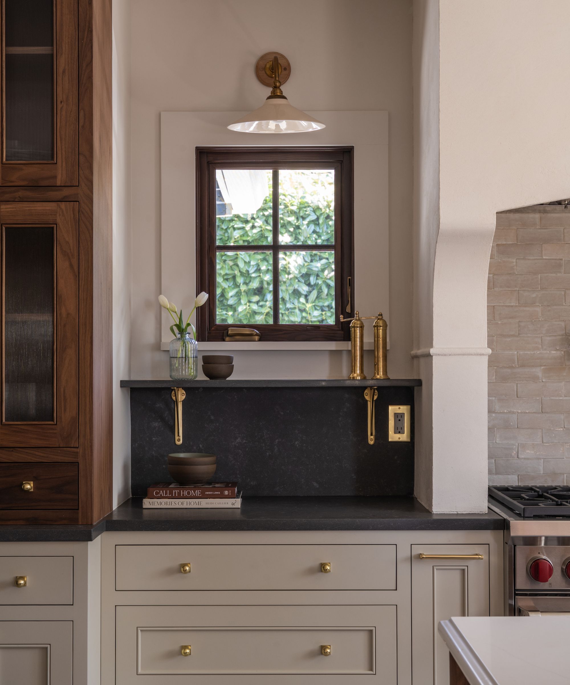 A wood and white kitchen with black countertops that continue into a backsplash and open shelves, supported by brass brackets
