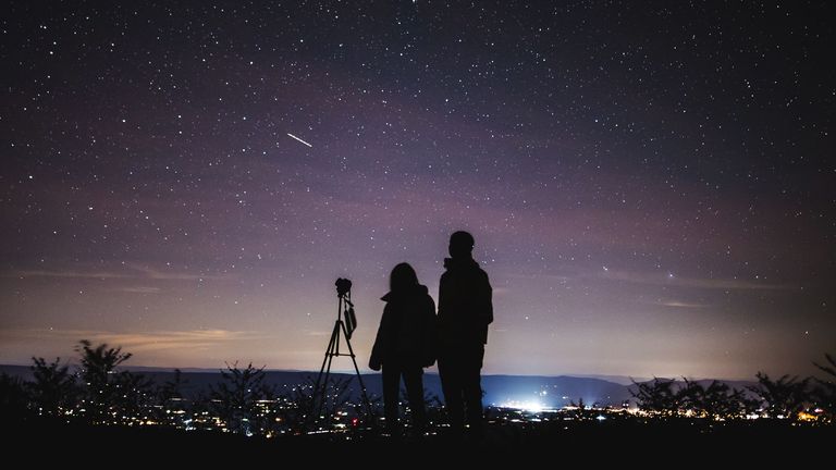 A couple with a telescope in silhouette against the night sky