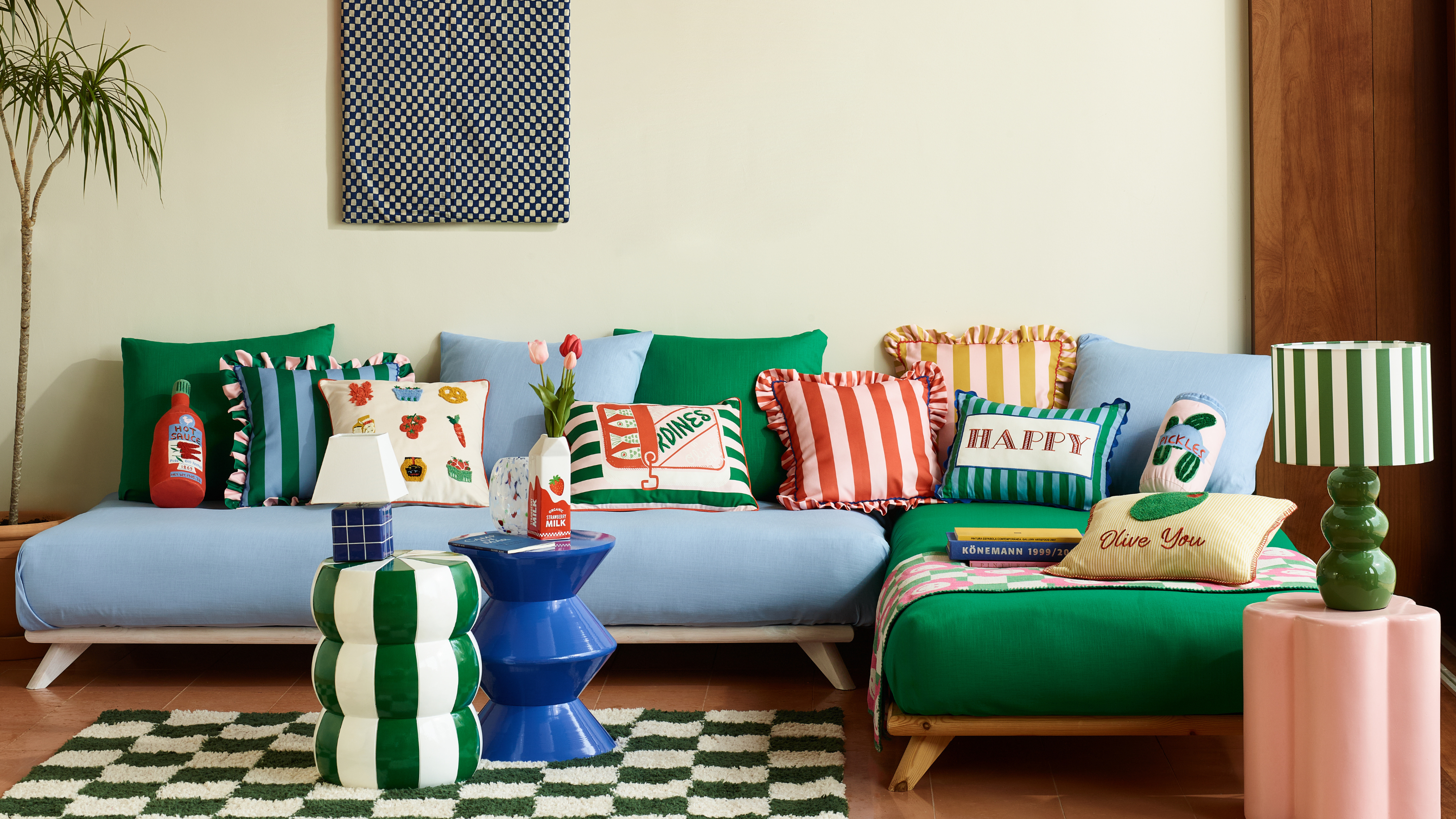 George Home new collection featuring lots of blue and green striped homeware positioned on a blue sofa in a modern living room.