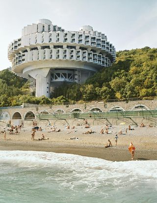 Photo of the Druzhba Sanatorium building in Ukraine above beach. The building is a large and circular and has many levels and windows.
