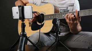 Man records his acoustic guitar using an iPhone and an external microphone