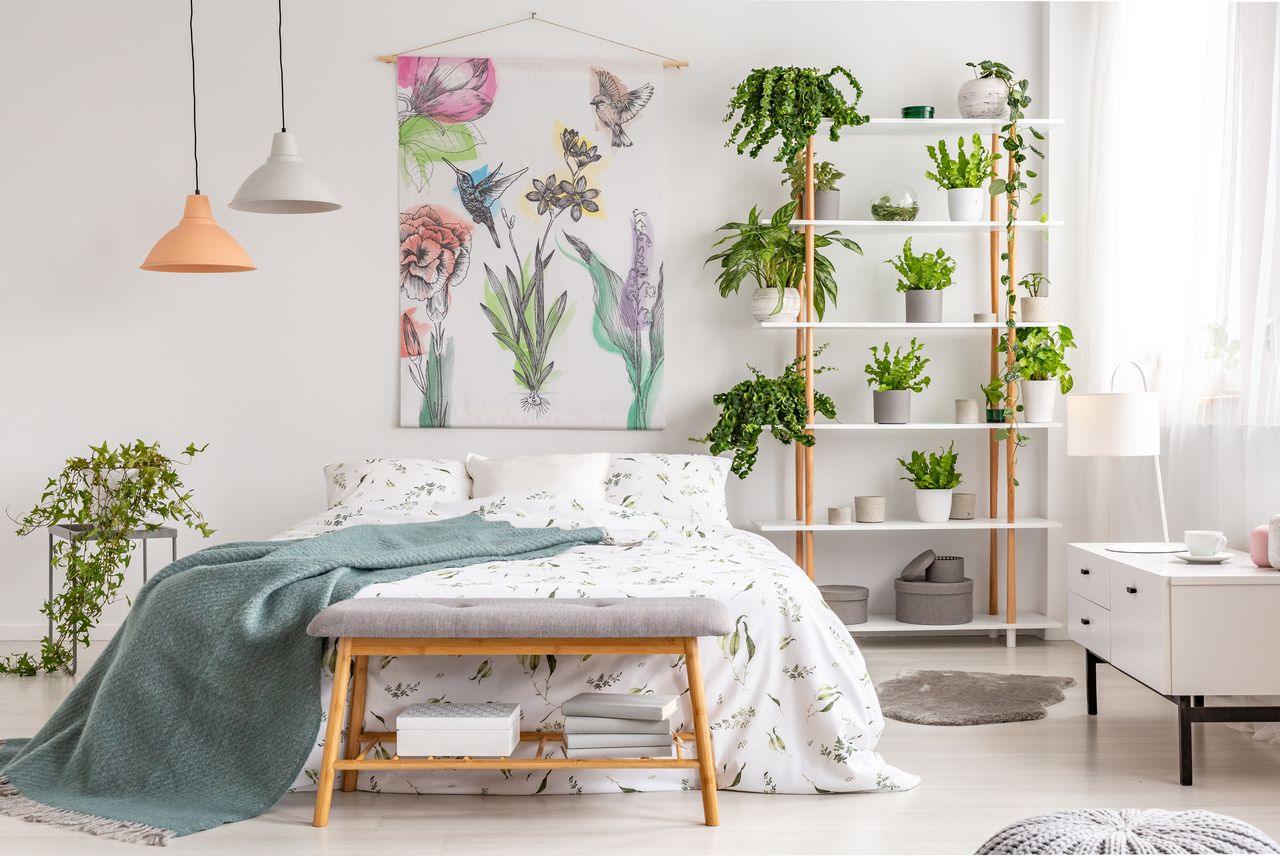 Bright airy small bedroom with low bed natural lighting and lots of green plants and clever storage shelves and ottomans Getty - KatarzynaBialasiewicz