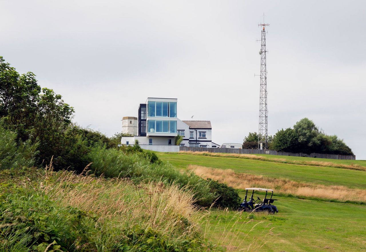 The coastal site of the build with grass covered headland and a lighthouse