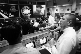 Mission Control in Houston celebrates the safe return of the Apollo 13 crew. Gene Kranz is smoking a celebratory cigar at the right while Deke Slayton, in front of the mission patch, shakes hands.