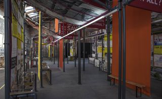 The People’s Museum, interior image, exhibition, orange divider screens, grey floor, artwork on the walls and ceiling, grey metal scaffolding framework