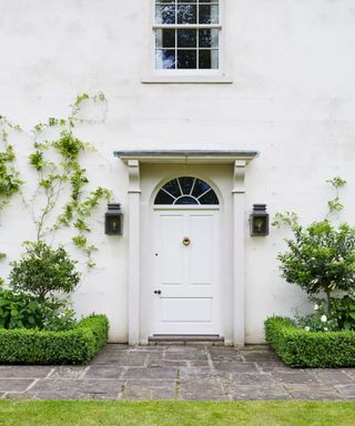 White building with white front door and some wall climbing plants