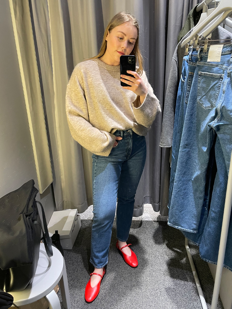 Woman in dressing room wears jumper, blue jeans and red flats