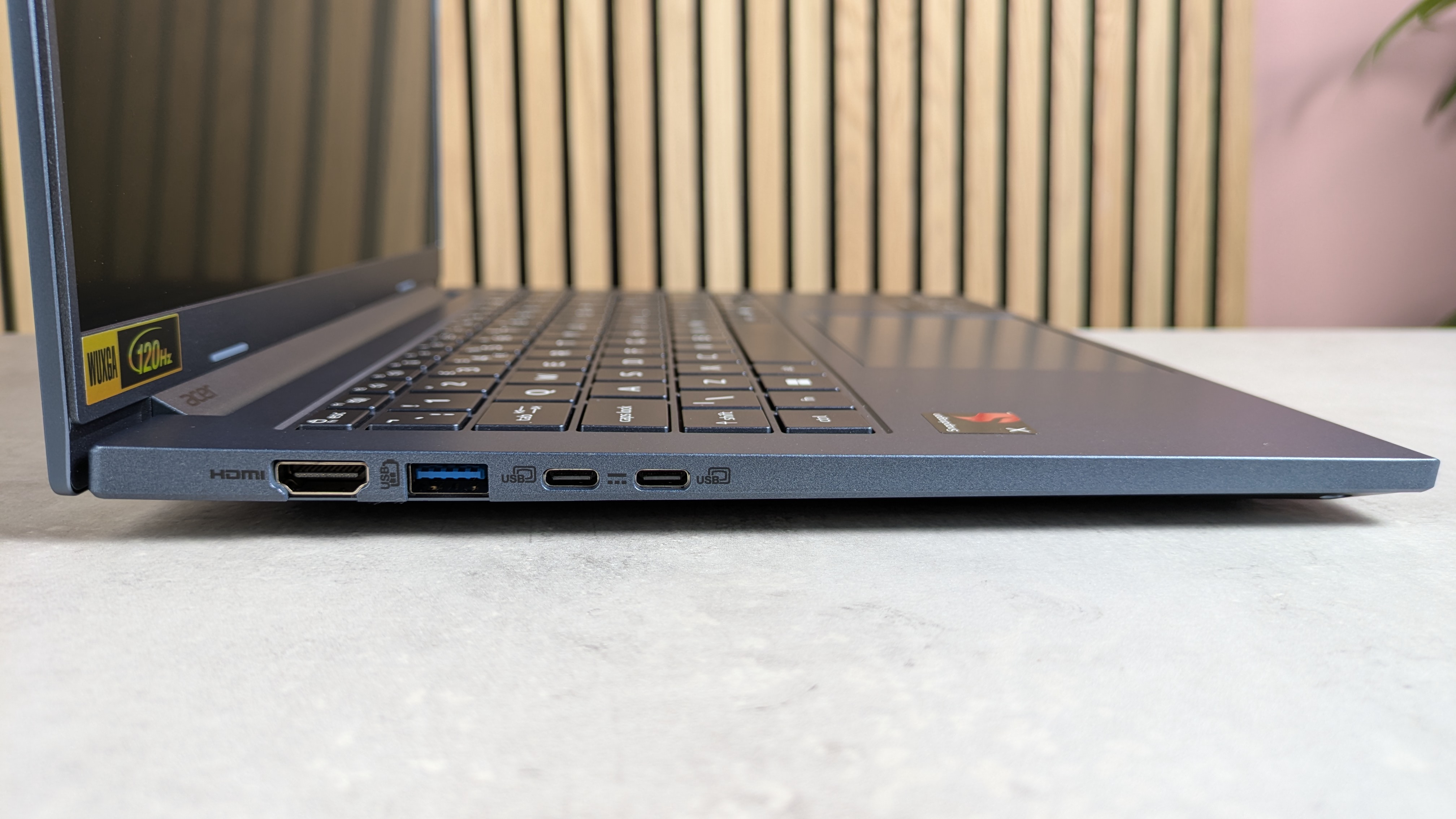 View of left-hand ports on Acer Aspire 14 AI (2025), open on desk with wooden panel, plant, and pink wall in background