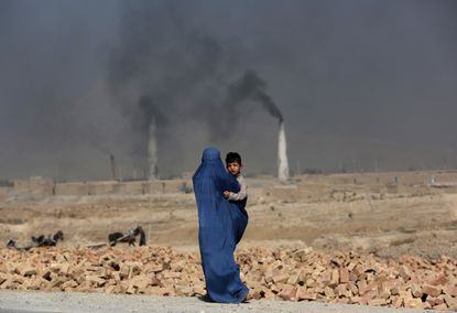 An Afghan woman walks past at a local brick factory as she carries her son, on the outskirts of Kabul, Afghanistan. 