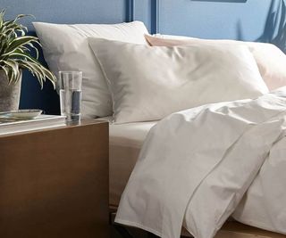 Brooklinen 100% Mulberry Silk Pillowcase on a bed beside a nightstand against a blue wall.