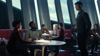 several people in Starfleet uniforms in a bar with space visible in windows behind them