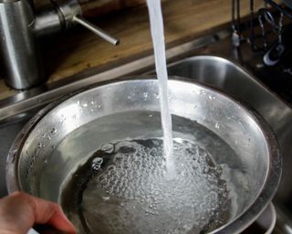 Big stainless steel bowl of water being filled under a kitchen tap