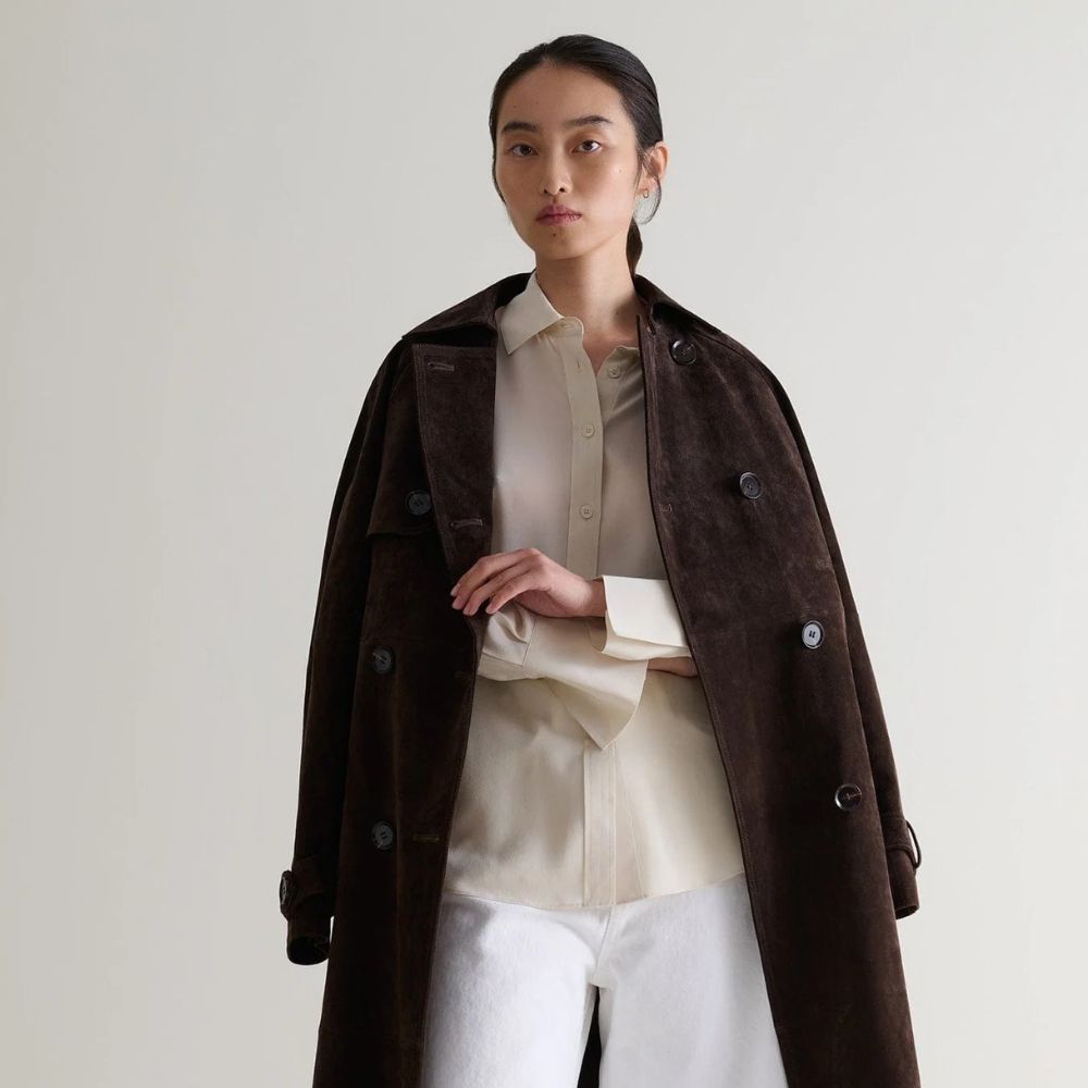 Woman wears suede brown trench coat, beige shirt and white jeans