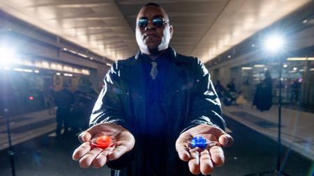 Comic Con attendee dressed as Morpheus from The Matrix gesturing to choose between red or blue pill.