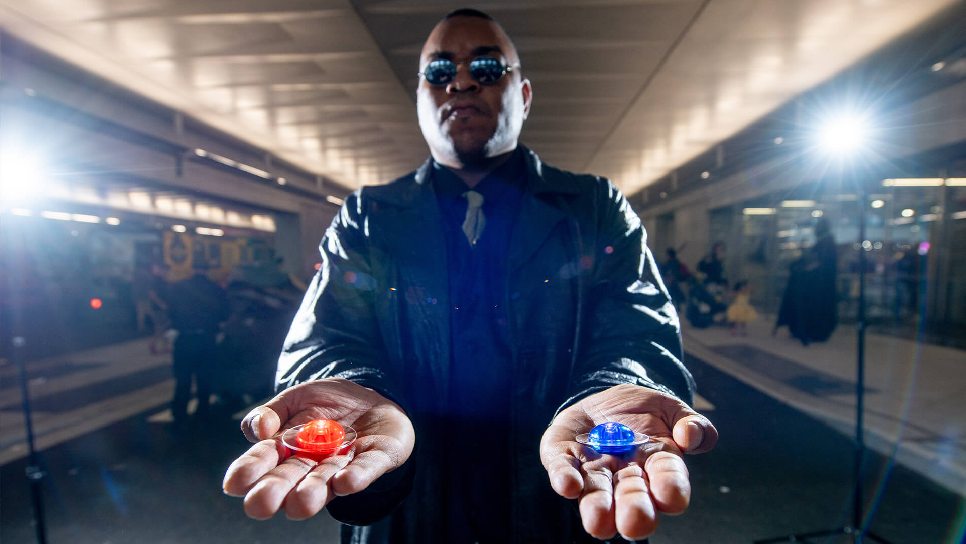 Comic Con attendee dressed as Morpheus from The Matrix gesturing to choose between red or blue pill.