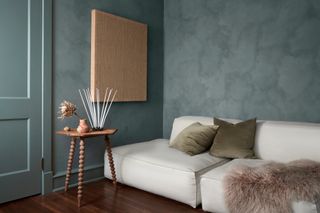 Living room with deep blue limewash walls, white sofa, canvas wall art and wooden bobbin side table