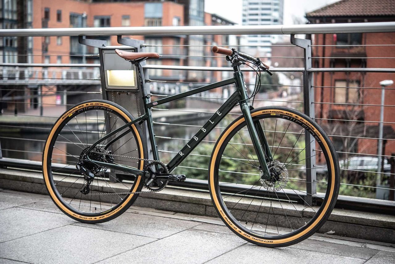 A dark green Ribble cycles hybrid al, with tan wall schwalbe tyres, leather saddle and grips, next to a canal in manchester, UK.