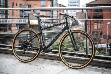 A dark green Ribble cycles hybrid al, with tan wall schwalbe tyres, leather saddle and grips, next to a canal in manchester, UK.