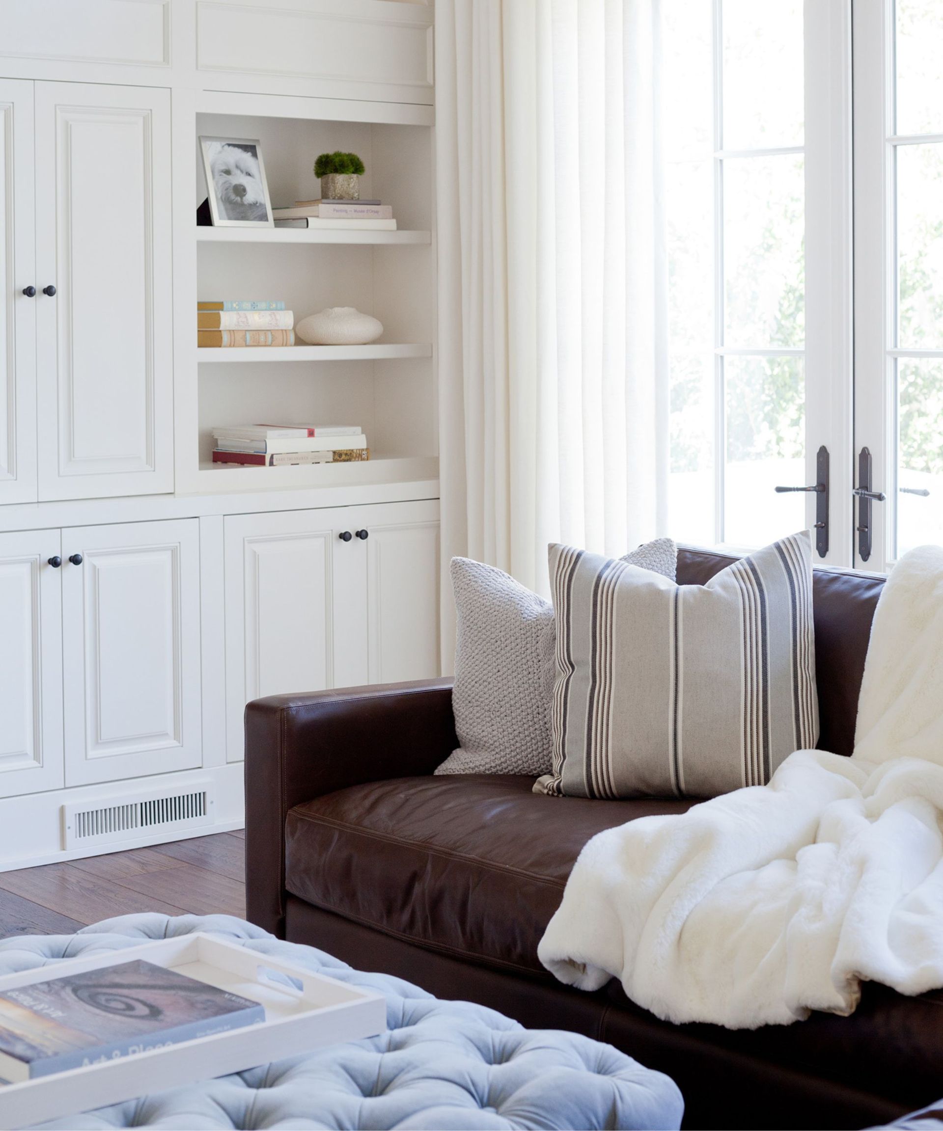 Corner of a white living room with a brown leather couch and pale blue futon