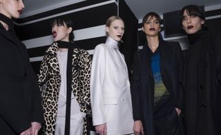 Five female models wearing looks from Bottega Veneta's collection. One model is wearing a black piece and neck scarf. Another model is wearing a leopard print coat, thin black scarf, off-white coloured jumper and white trousers. The third model is wearing a white jacket and light coloured neck scarf. And the last two models are wearing dark jackets with one wearing a dark coloured scarf and the other wearing a black top with colour gradient design and black trousers