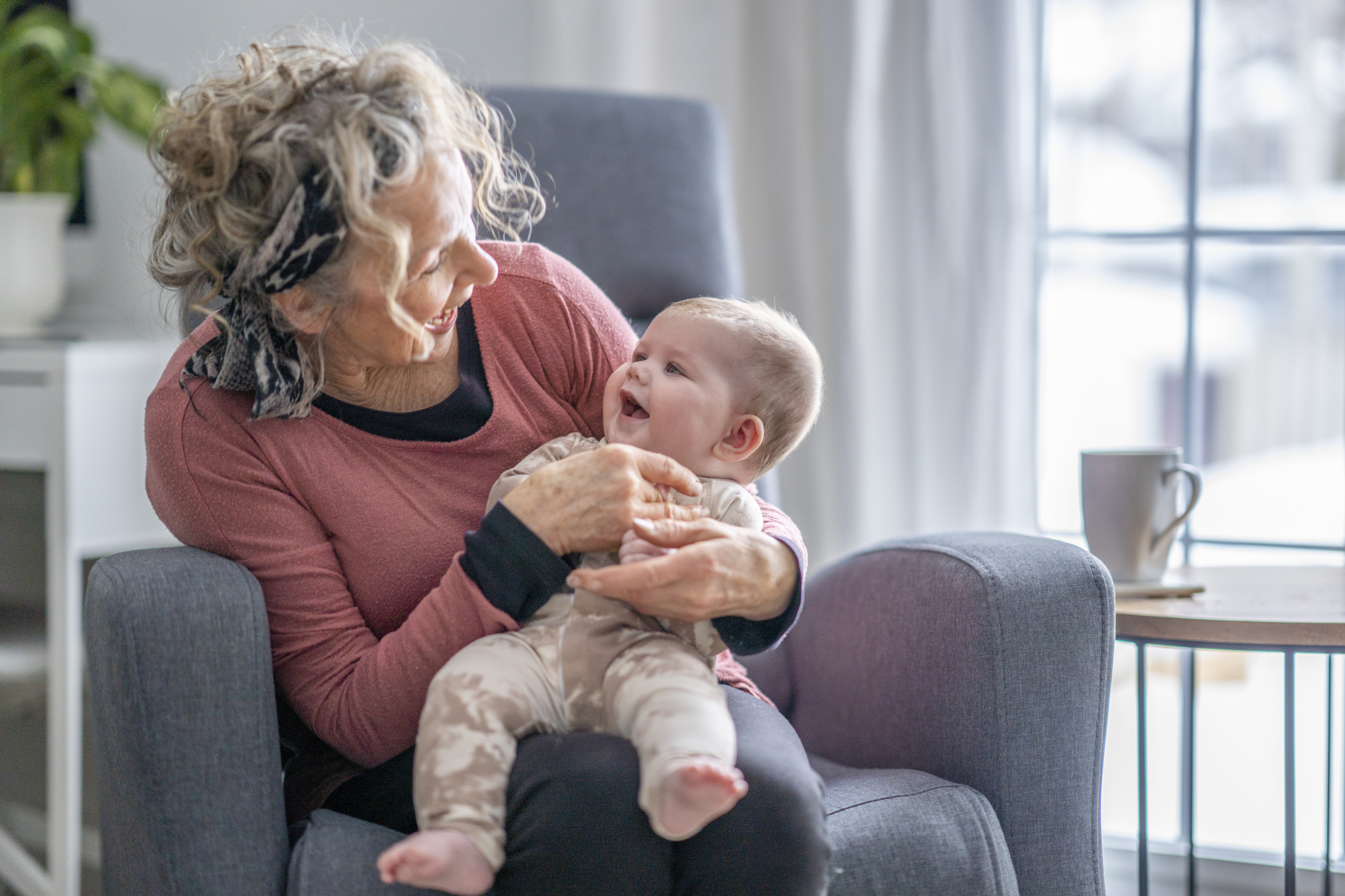 A grandmother and her baby granddaughter are looking at eachother and laughing.