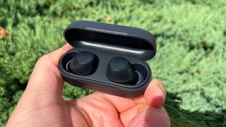 Sony WF-C510 in-ear headphones in case held in hand with grassy lawn in background