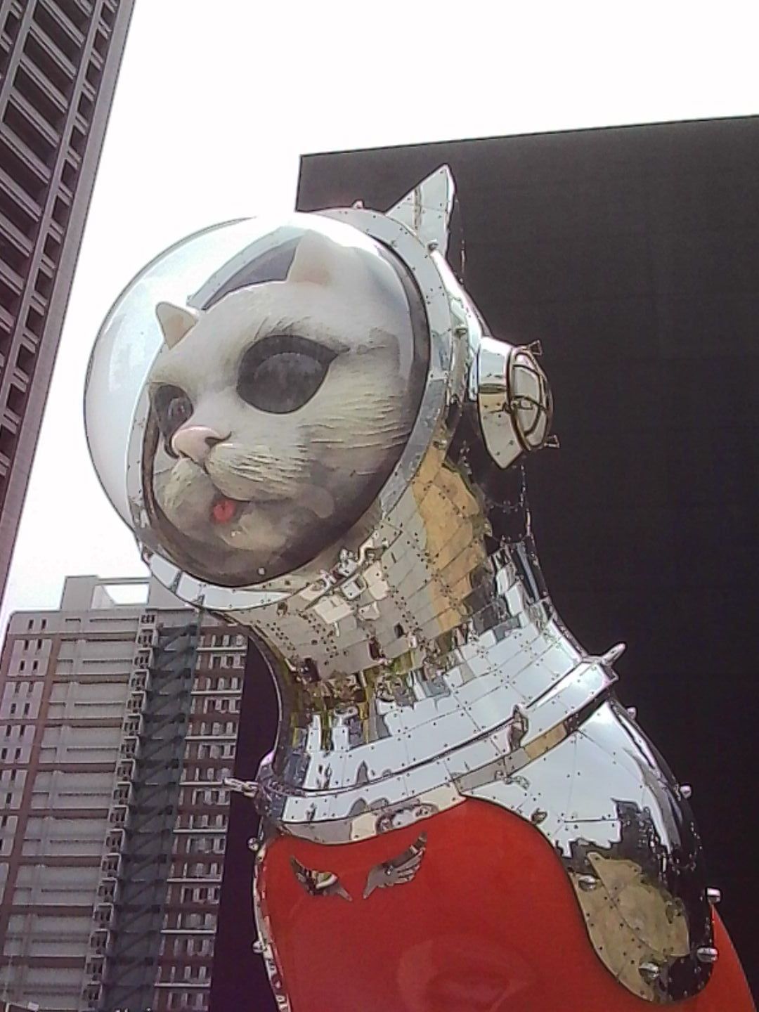 Large metallic cat sculpture wearing a space helmet outside an urban building in Japan.