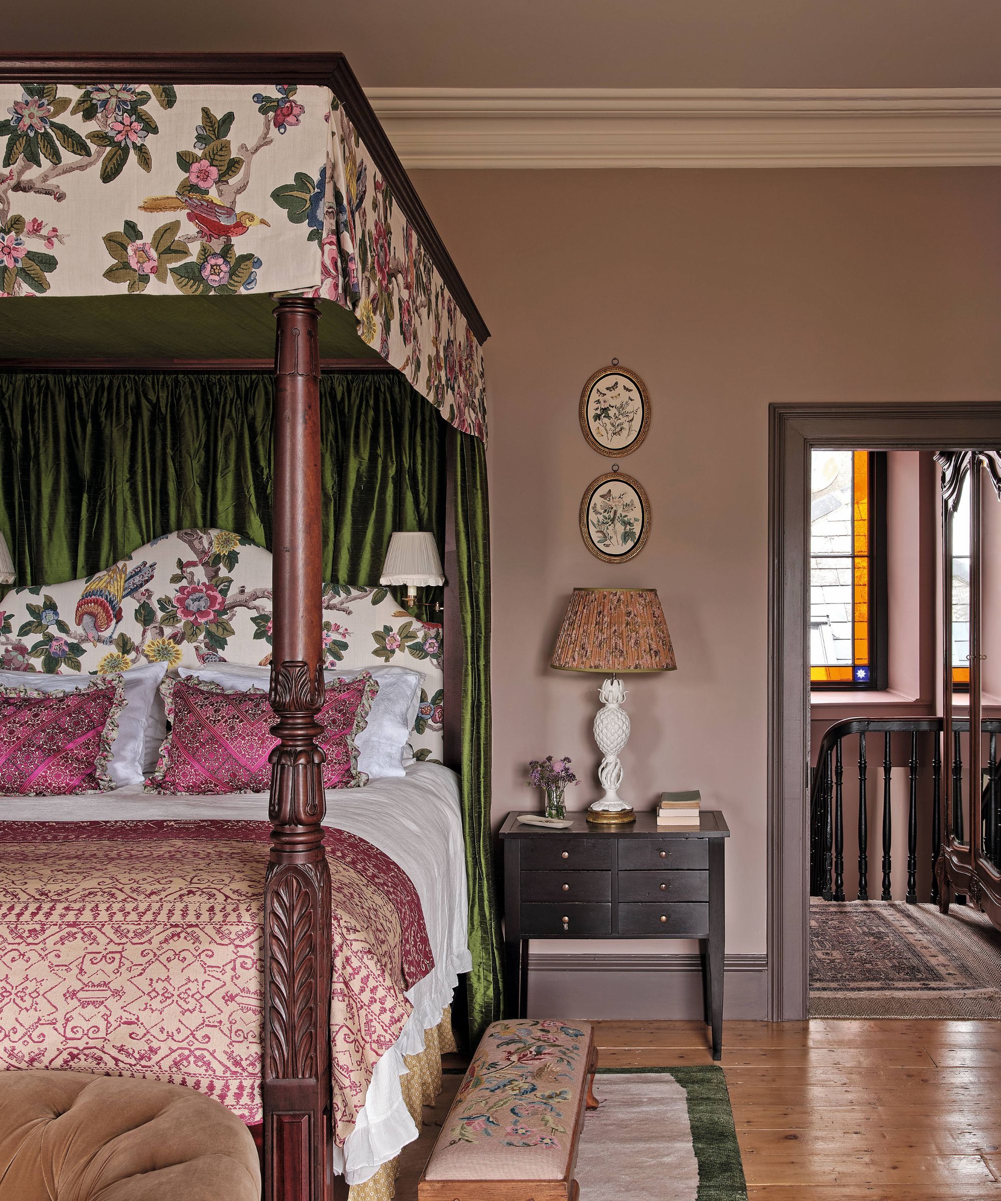 a moody mauve bedroom with antique four posted wooden bed with floral canopy and layered patterned linens
