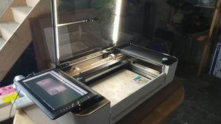 The Glowforge Pro review shows a laser cutter machine on a table, with it's lid open