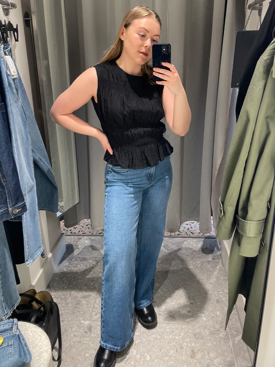 Woman in dressing room wears blue jeans, black top and boots