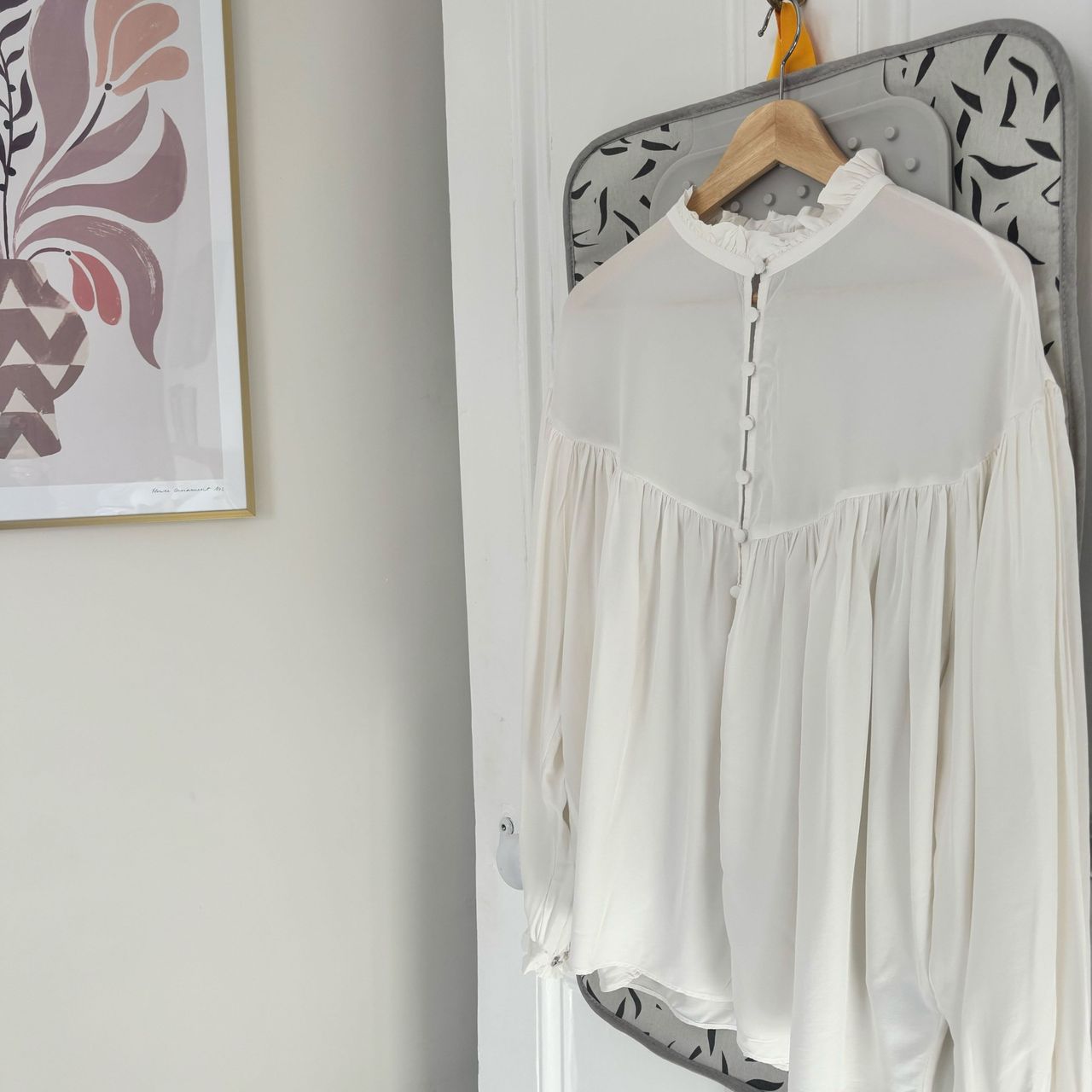 steamed white blouse hanging on a door with artwork on wall