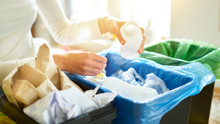 Person putting a plastic container into a recycling bin with blue bag inside