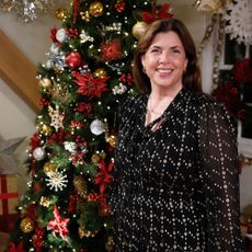 Kirstie Allsopp in a dark dress in front of a Christmas tree