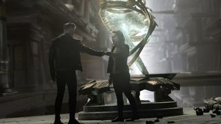 two people in leather jackets stand on a carved stone platform inside a massive prison-like structure next to a swirling, glowing green statue resembling a helix shape