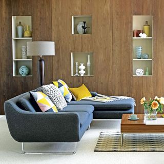Living room with wooden wall with built-in shelves neutral carpet wooden coffee table and grey sofa