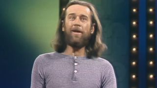 George Carlin, long brown hair and grey shirt, performing standup, footage used in HBO's doc George Carlin's American Dream