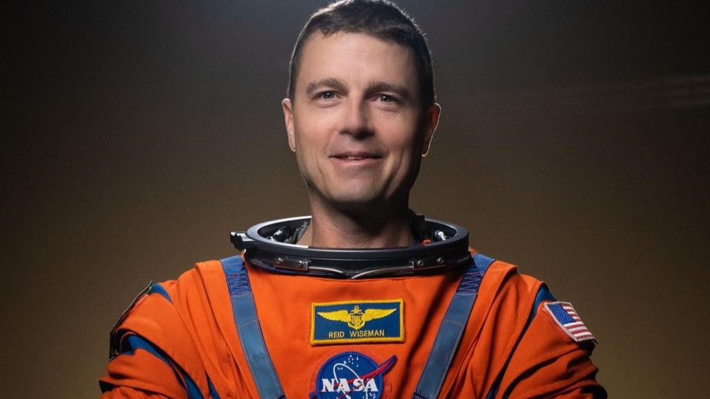 a man wears an orange spacesuit with no helmet.