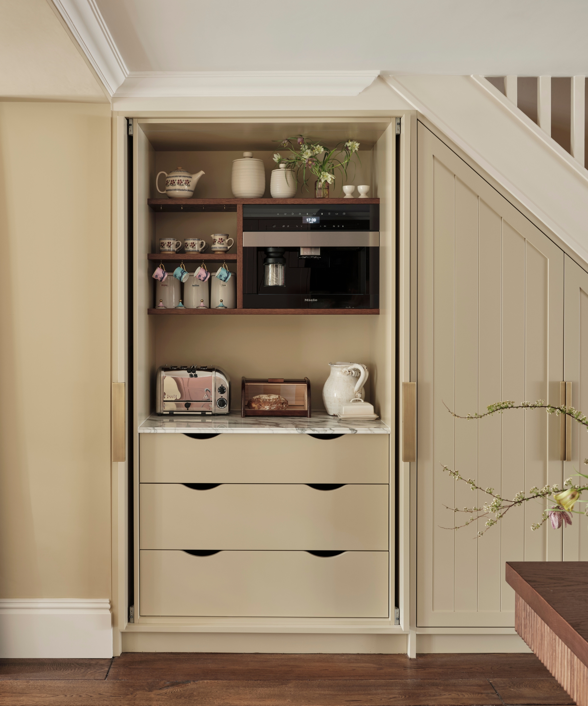 A warm neutral under-stairs pantry used as a breakfast station, featuring pocket doors for ease of use