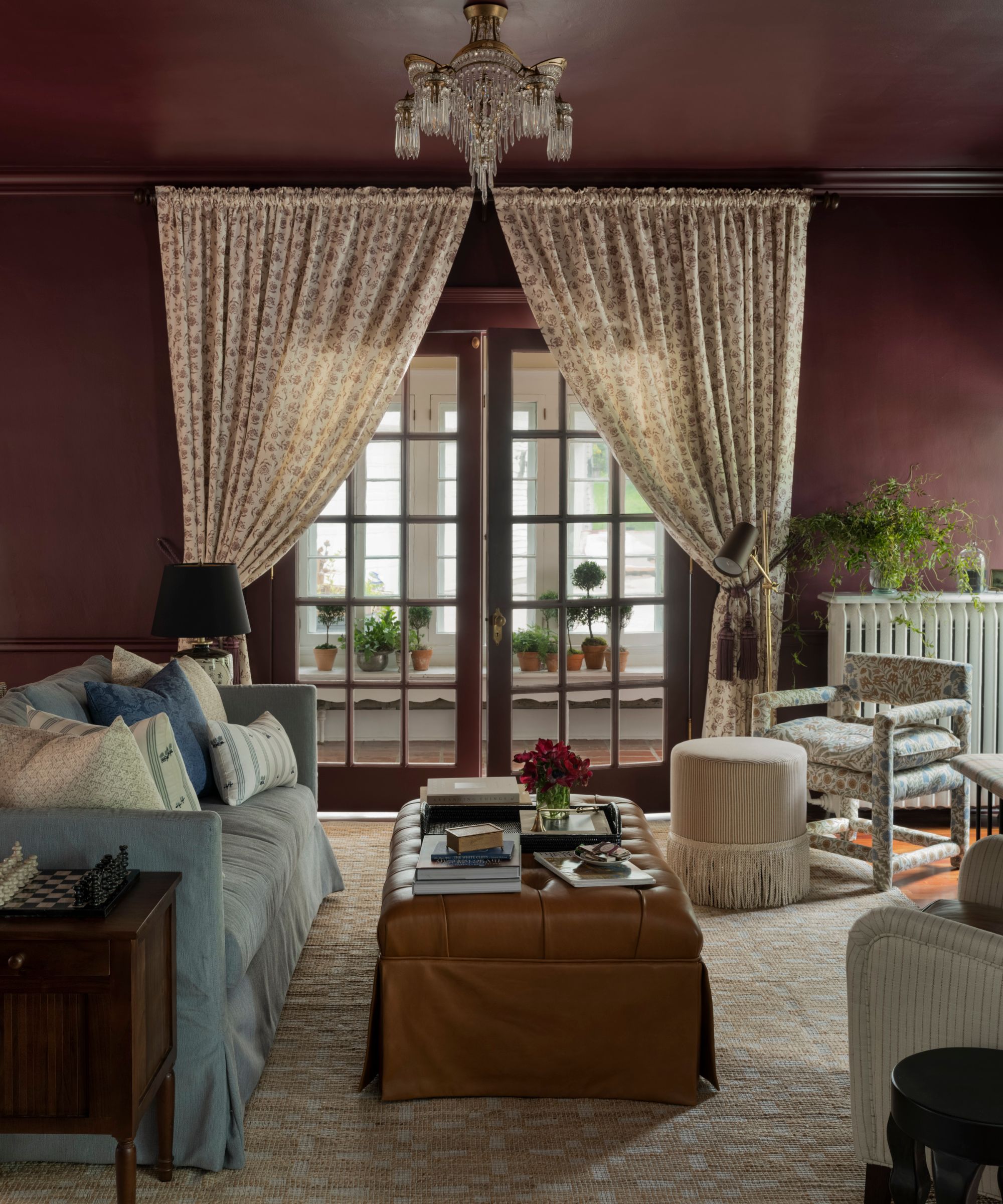 dark purple color drenched living room dressed with a light blue couch, leather ottoman, floral armchairs and drapes