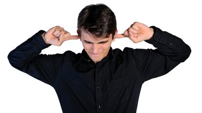 A man puts his fingers in his ears because he doesn't want to hear something.
